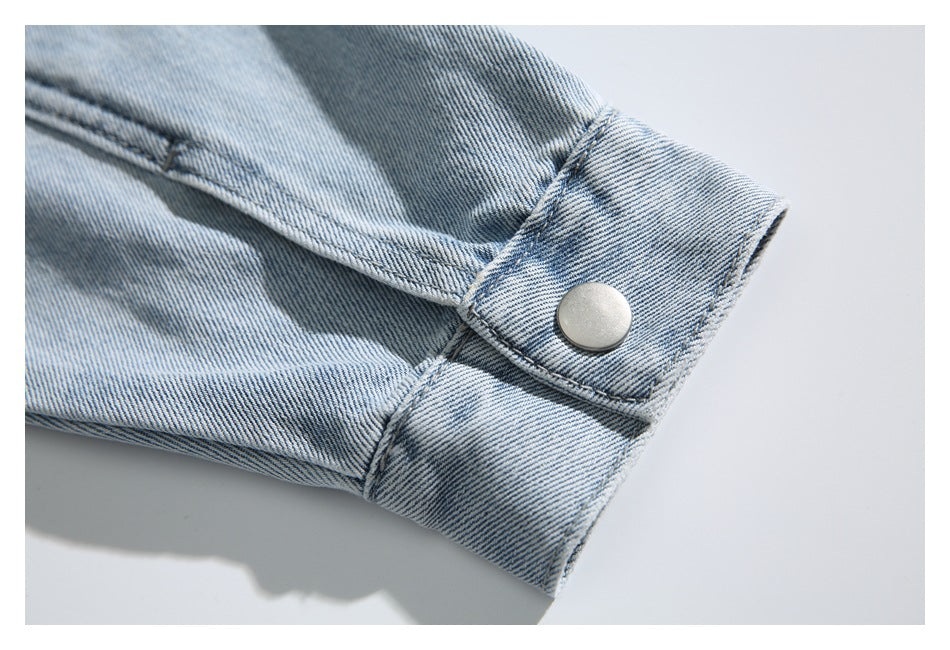 Close-up of a light blue denim cuff with a silver snap button and stitched edge.