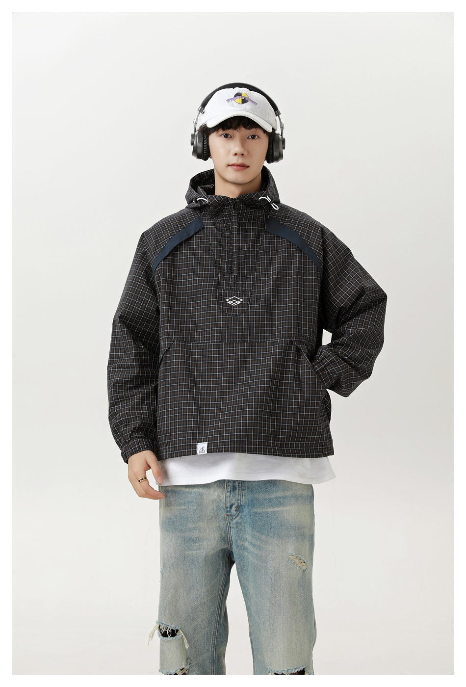 Front view of a model wearing a dark grid-plaid hooded pullover jacket with a large front pouch pocket.