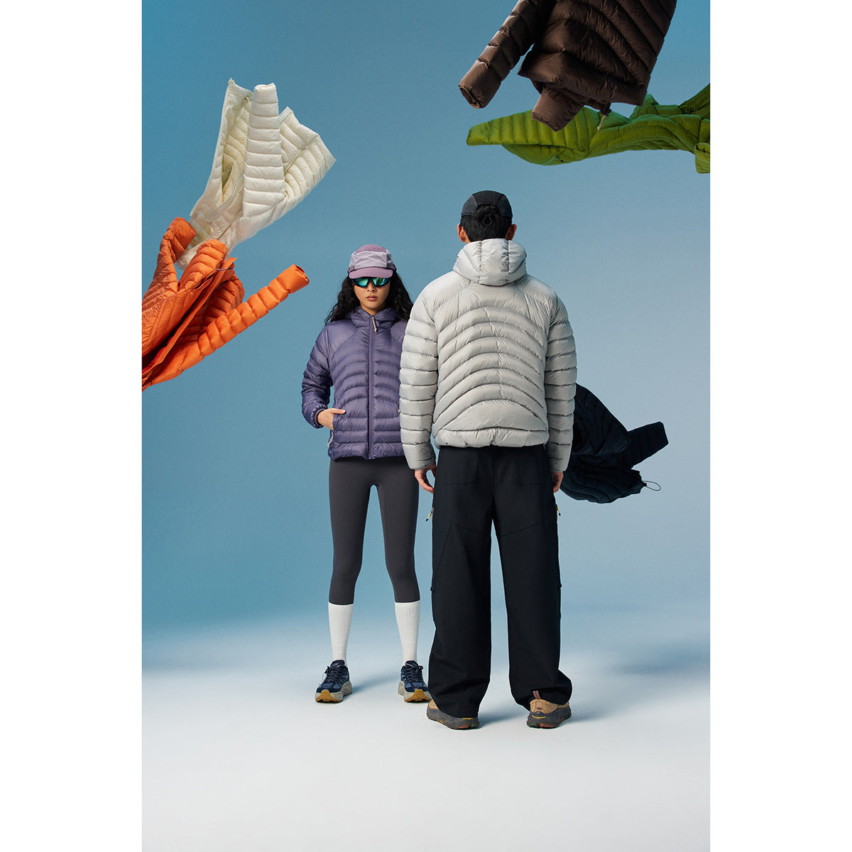 Two models in purple and light gray hooded puffer jackets, with colorful jackets floating around them.