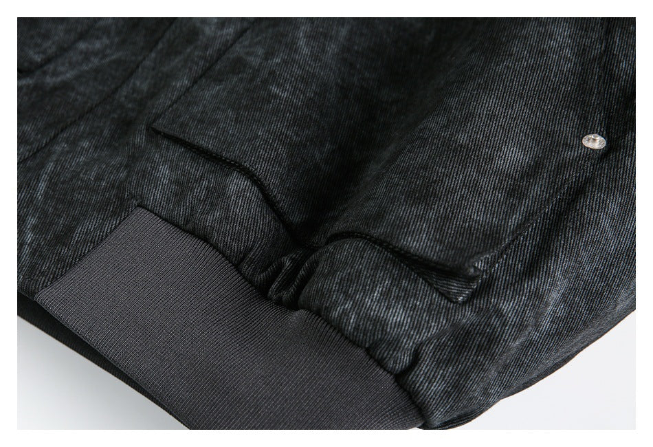 Close-up of a dark jacket's snap-fastened pocket flap above a wide ribbed hem band.