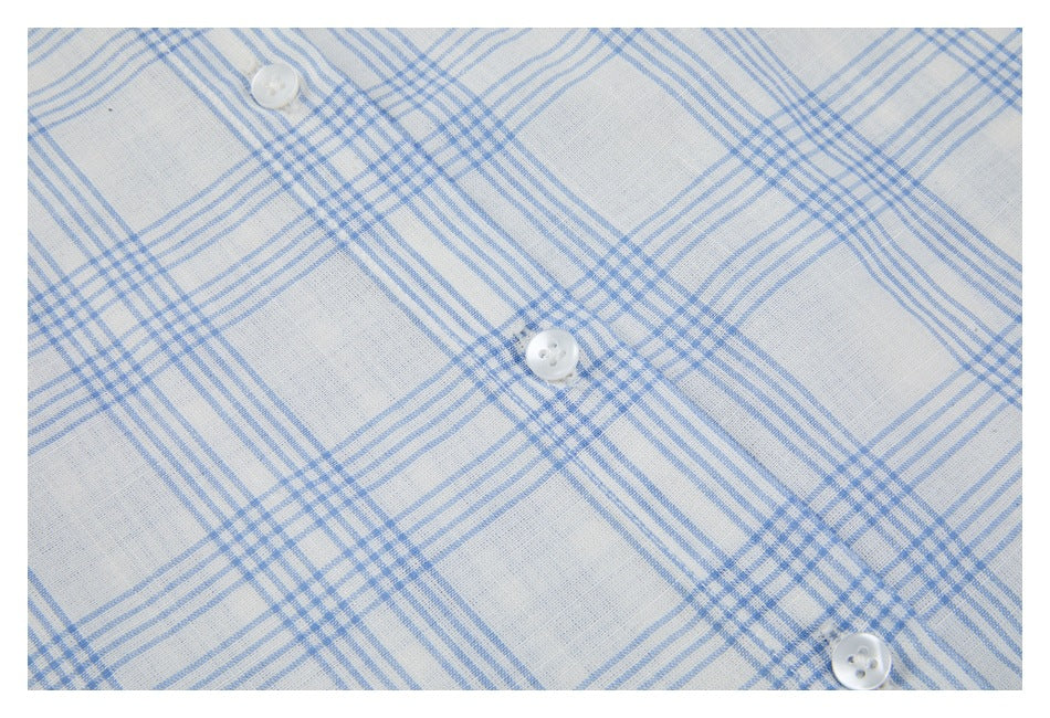 Close-up of white shirt fabric with a light blue plaid pattern and several white buttons.