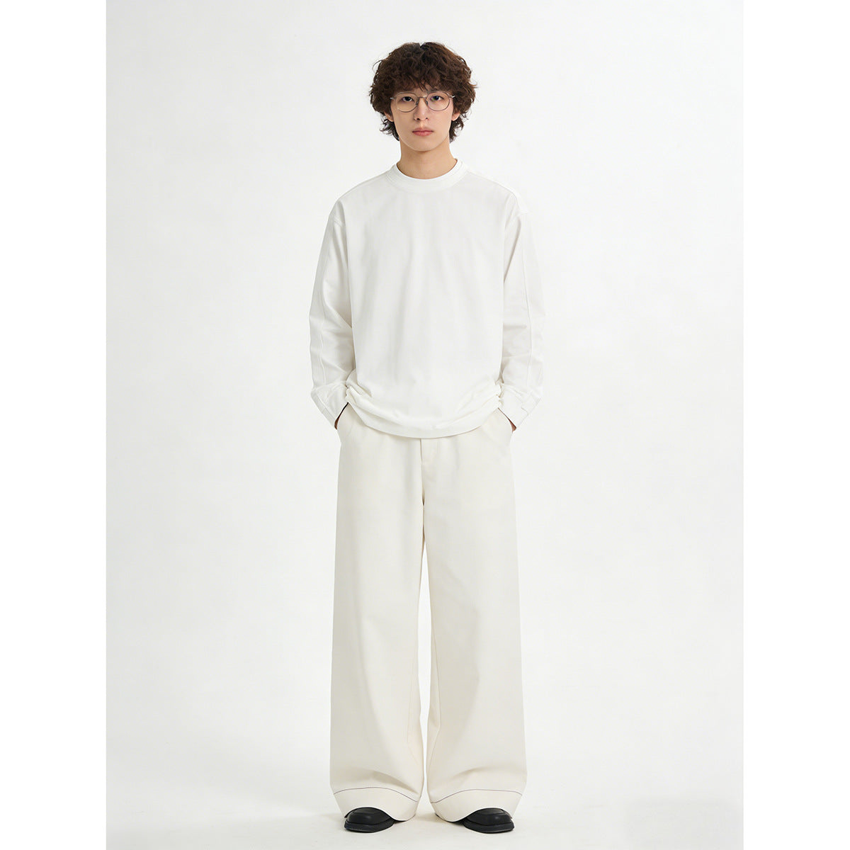 Model wearing a plain white crewneck sweatshirt and very wide-leg trousers, shown full length from the front.