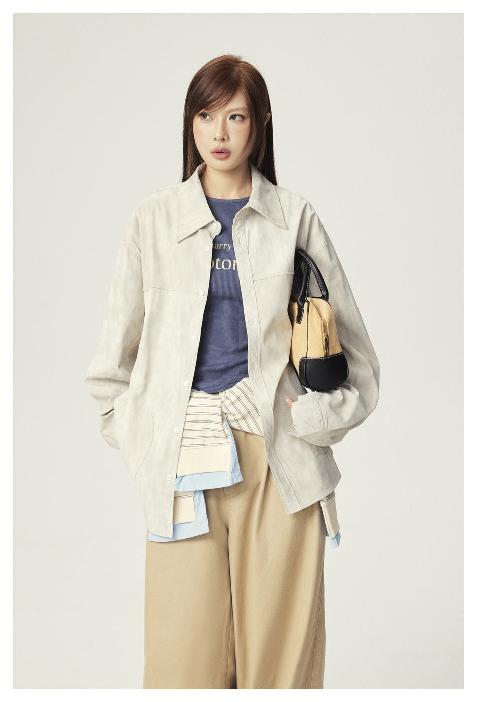 Model wearing an oversized light beige button-front shirt jacket over a blue top, with tan trousers and a two-tone bag.