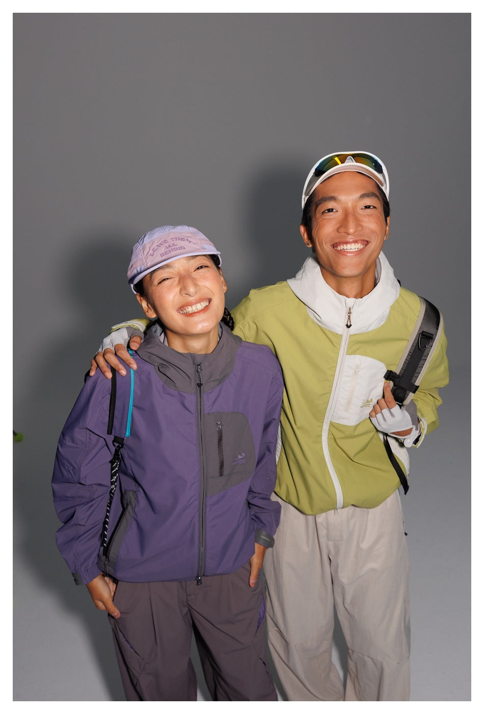 Two models wear color-blocked outdoor jackets: one purple and charcoal, the other lime green and white.