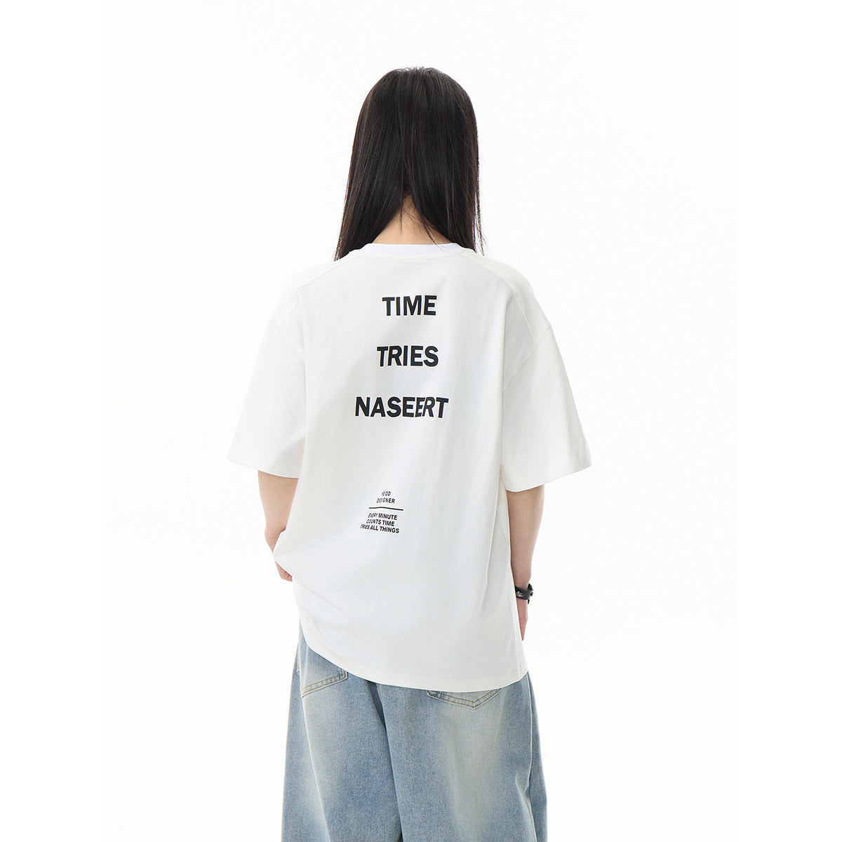 Back view of a model wearing a white oversized T-shirt with large stacked black text and smaller text below.