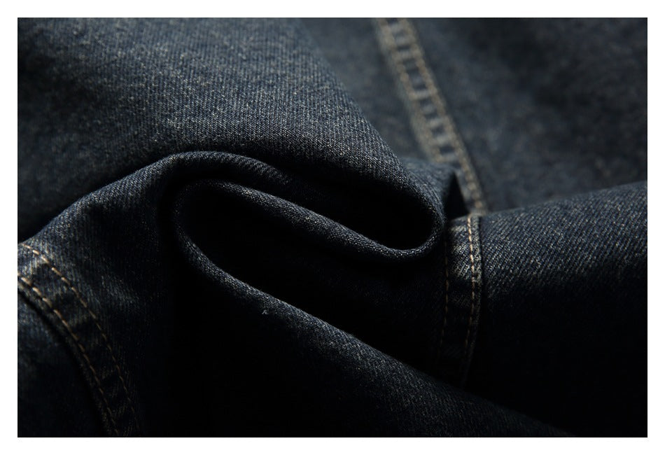 Close-up of dark indigo denim folded into a soft ridge, with visible tan-stitched seams.