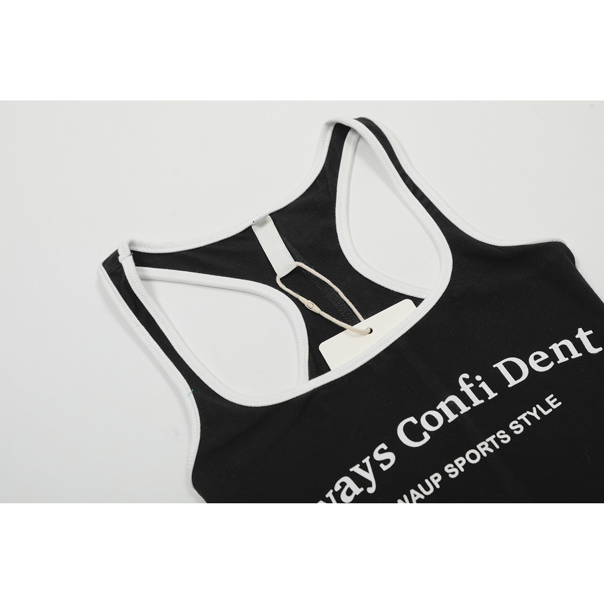 Close-up of a black racerback tank top with white trim, a hangtag, and partially visible white lettering.