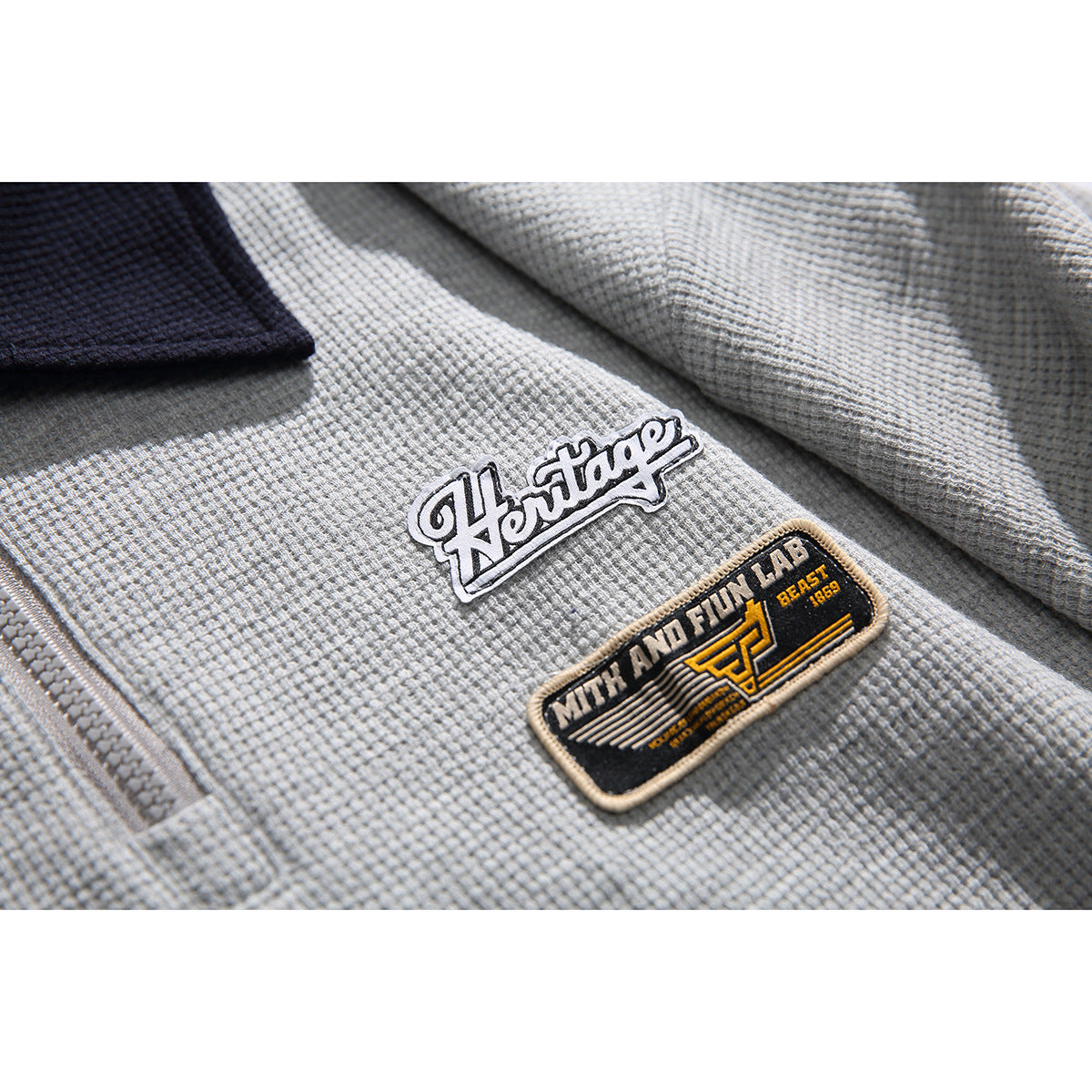 Close-up of the gray polo’s textured fabric, zipper edge, dark collar, and embroidered chest patches.
