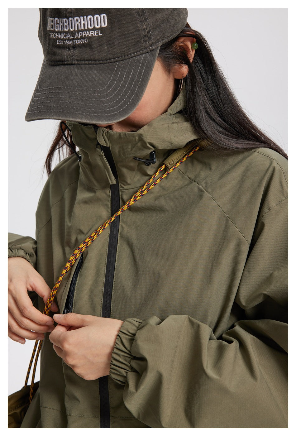 Close-up of an olive jacket showing its high collar, front zipper, pocket, and elastic cuff.