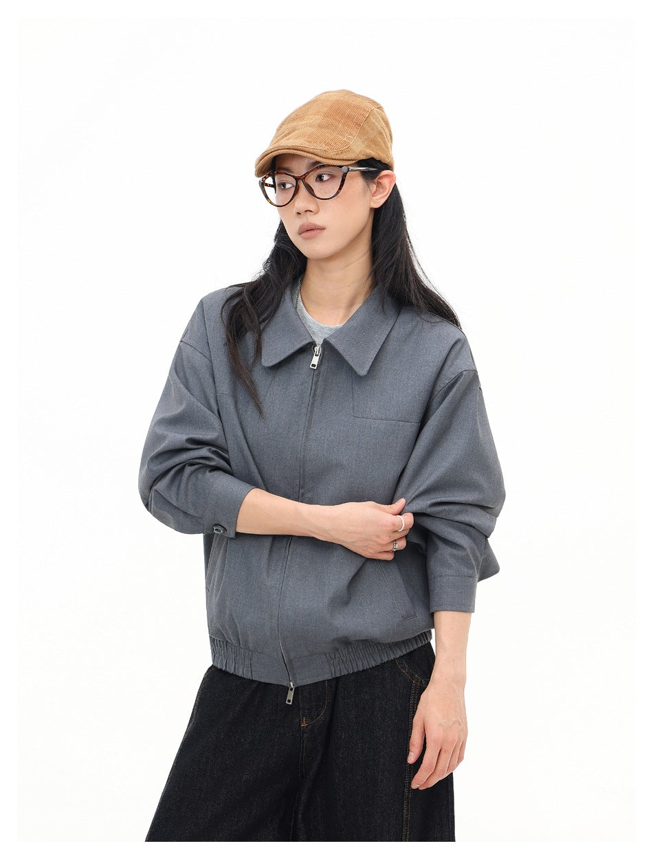 Model in a gray zip jacket with wide collar and sleeves pushed up, shown from a three-quarter angle.