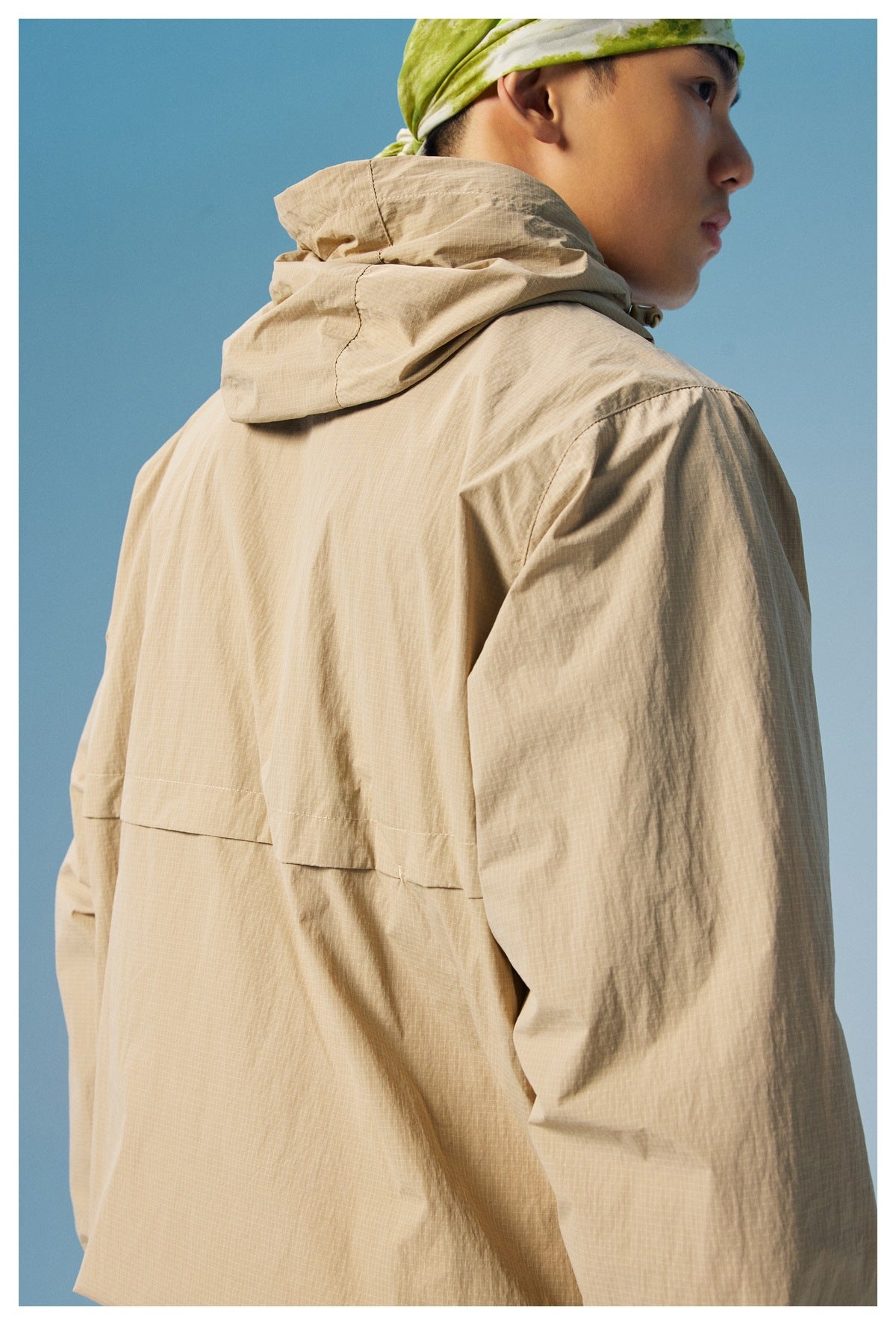 Close rear view of a model wearing a beige hooded pullover jacket against a blue background.