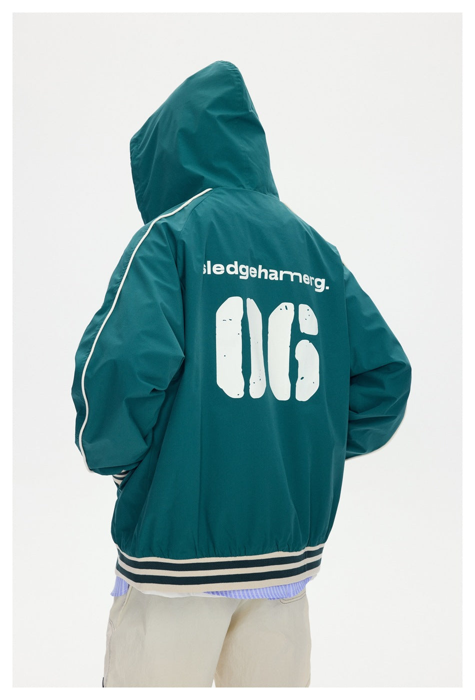 Rear view of a hooded teal jacket with cream piping, striped hem and large white lettering and graphics on the back.