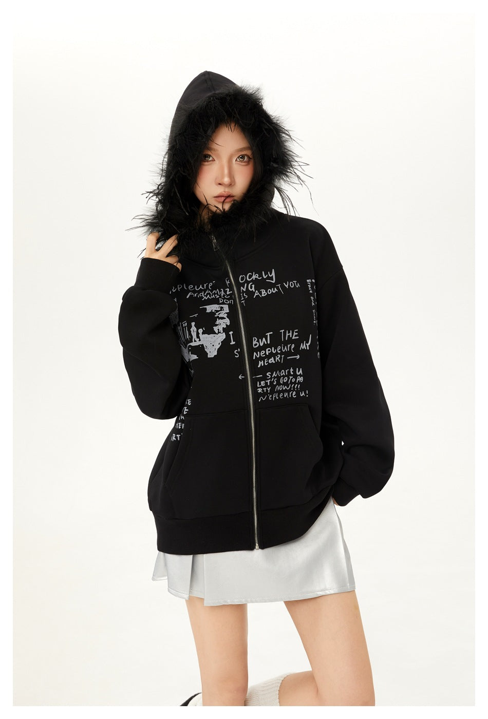 Model wearing a black zip hoodie with fur-trimmed hood and gray text print, paired with a silver skirt.
