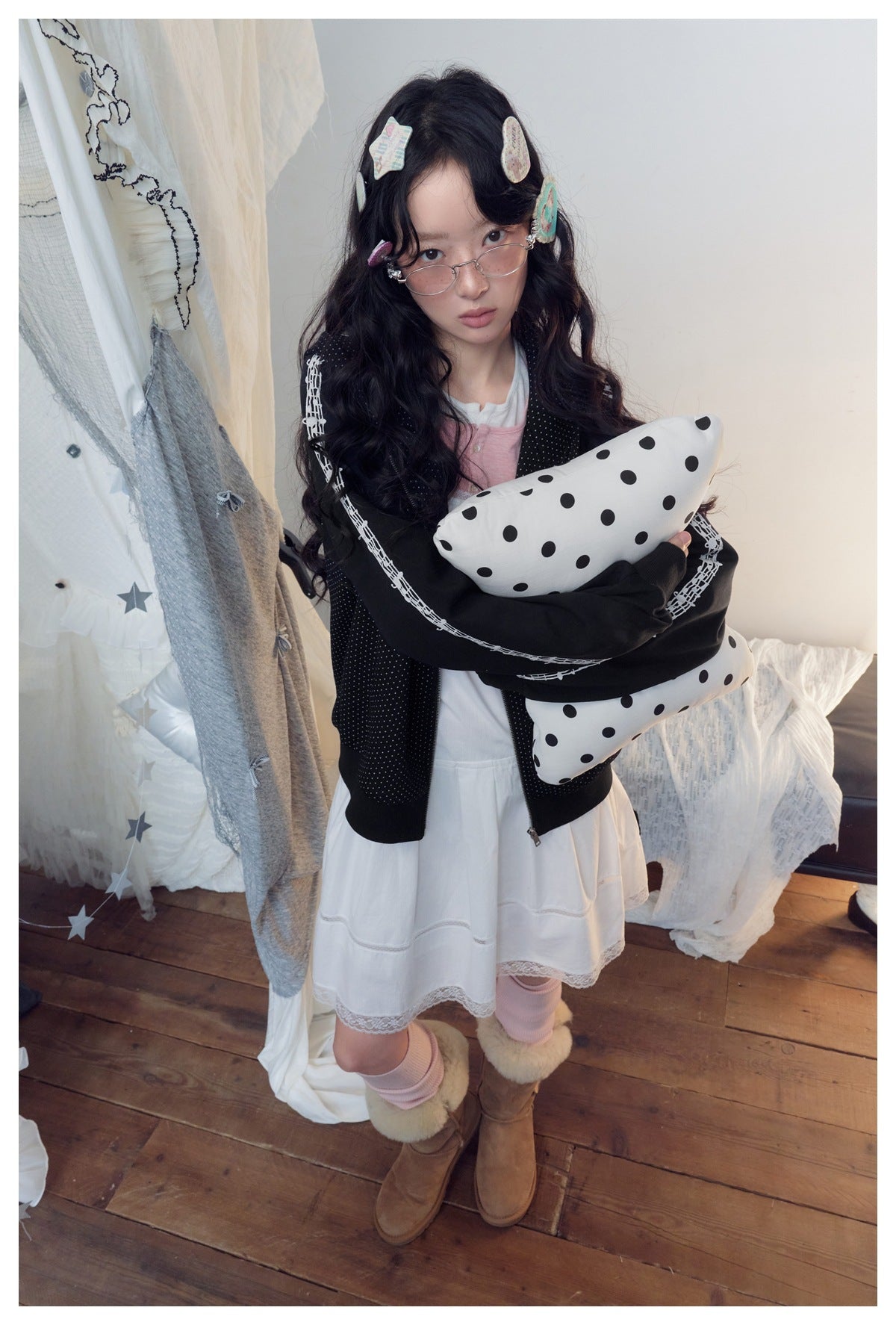 Model wearing the black polka-dot zip hoodie over a white dress, holding a polka-dot pillow
