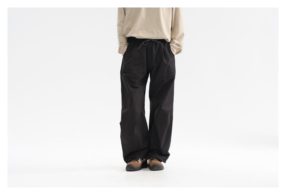 Rear view of a person wearing loose black drawstring pants with wide legs and a beige top.