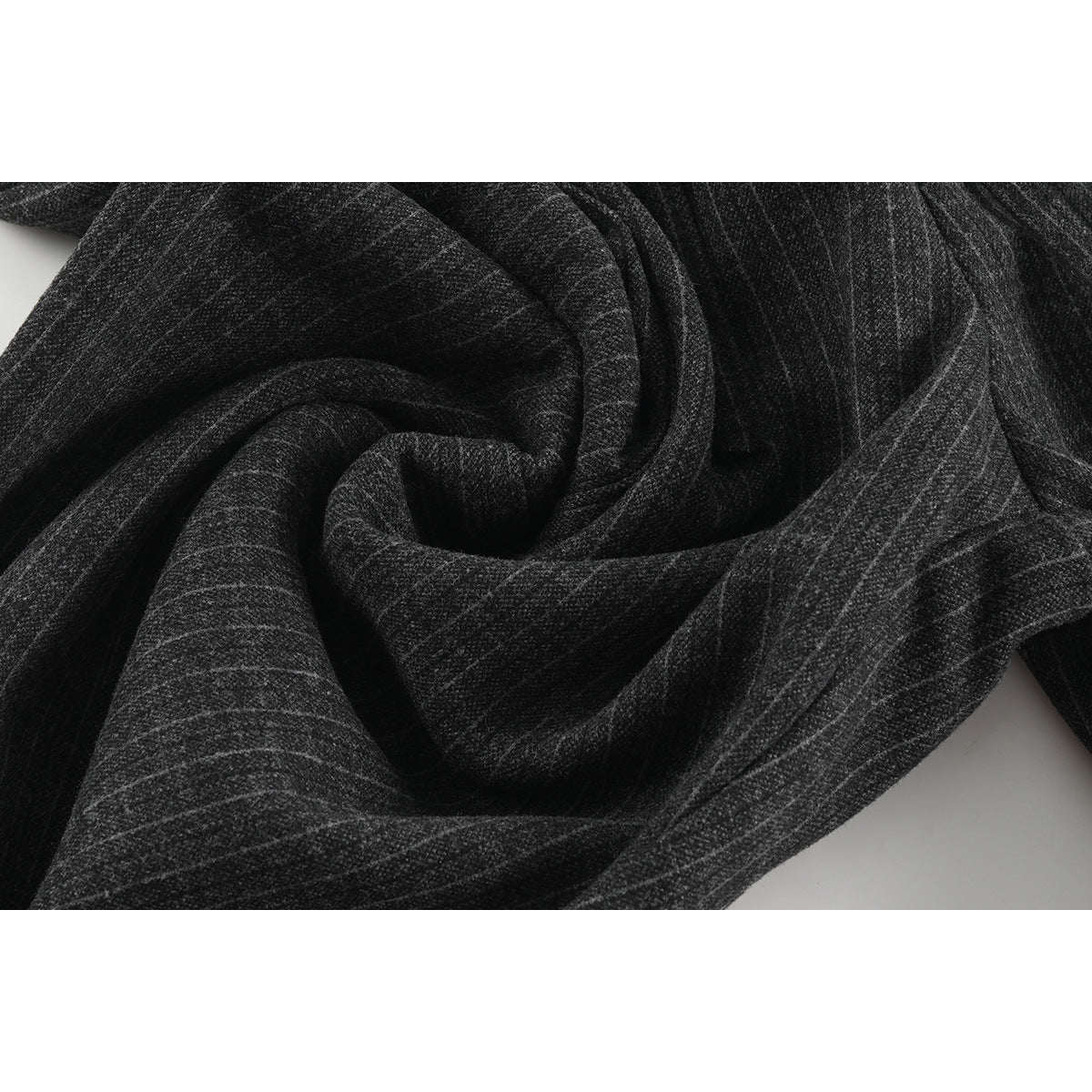 Close-up of charcoal pinstripe trouser fabric arranged in soft folds.