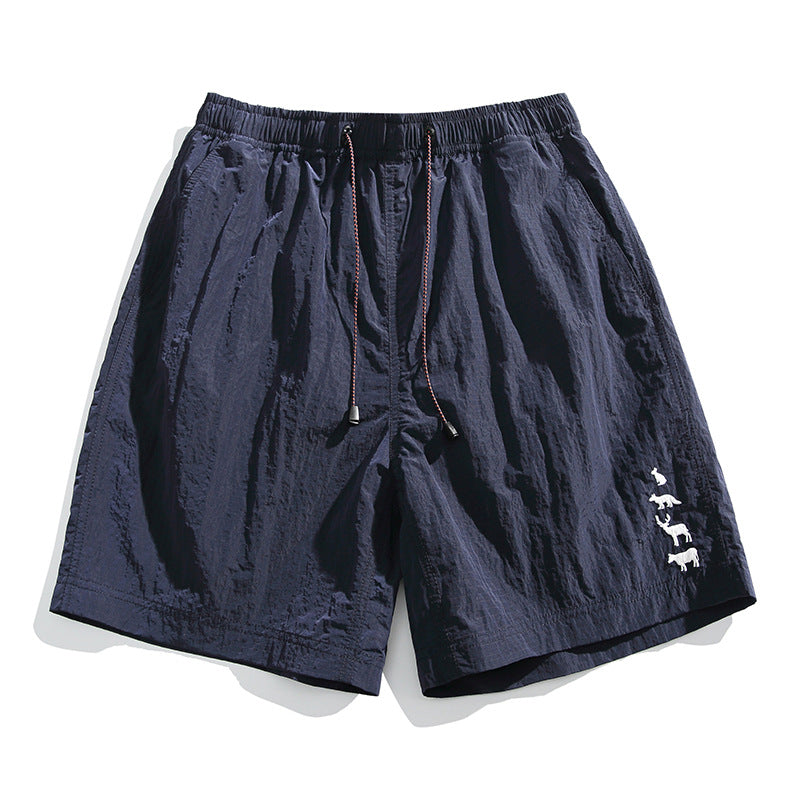 Navy blue crinkled drawstring shorts with elastic waist and white animal embroidery on the lower leg, flat lay