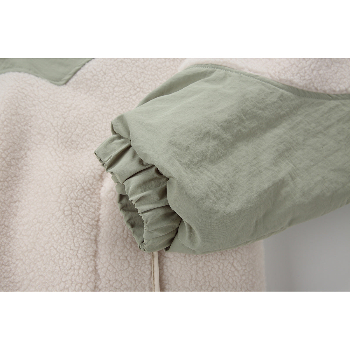Close-up of a sage-green sleeve cuff and gathered finish against cream fleece.