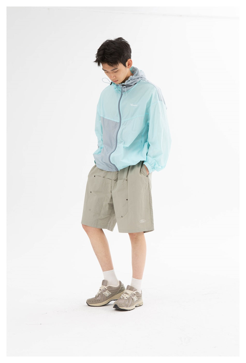 Model wearing gray knee-length shorts with front patch pockets, a light blue hooded jacket and gray sneakers