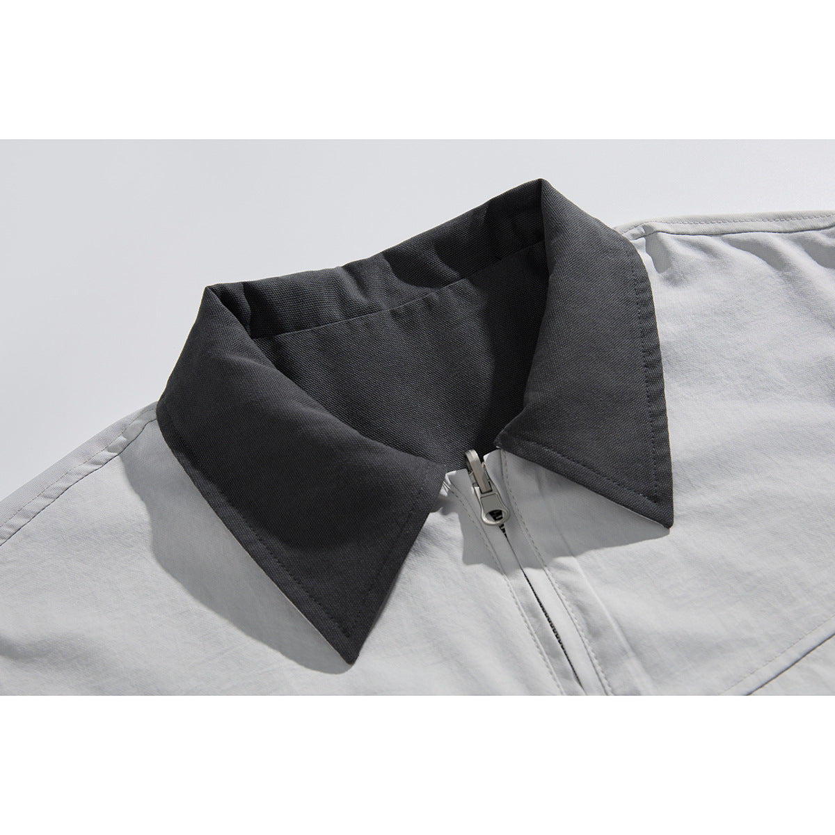 Close-up of a light gray jacket with a dark charcoal pointed collar and front zipper.
