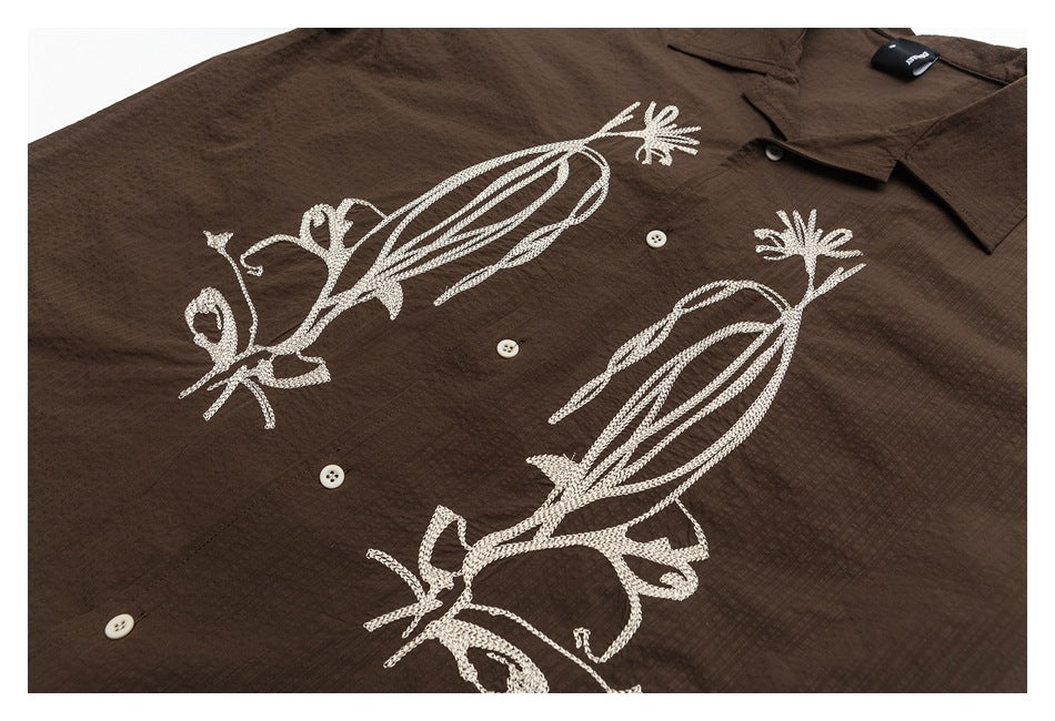 Dark brown button-up shirt front with large cream embroidered bird designs, shown close up.