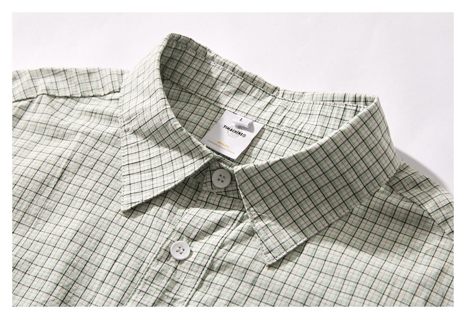 Close-up of a pale green and white plaid shirt collar, neckline label, and front buttons.