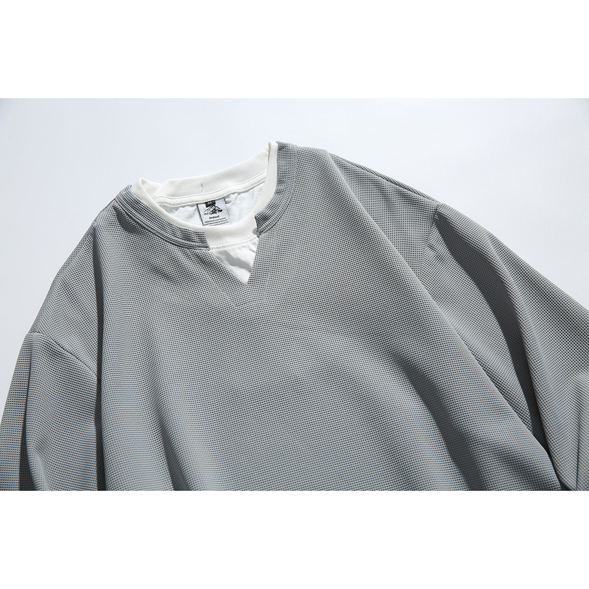 Close-up of a gray textured long-sleeve top with a notched neckline and white layer visible underneath.