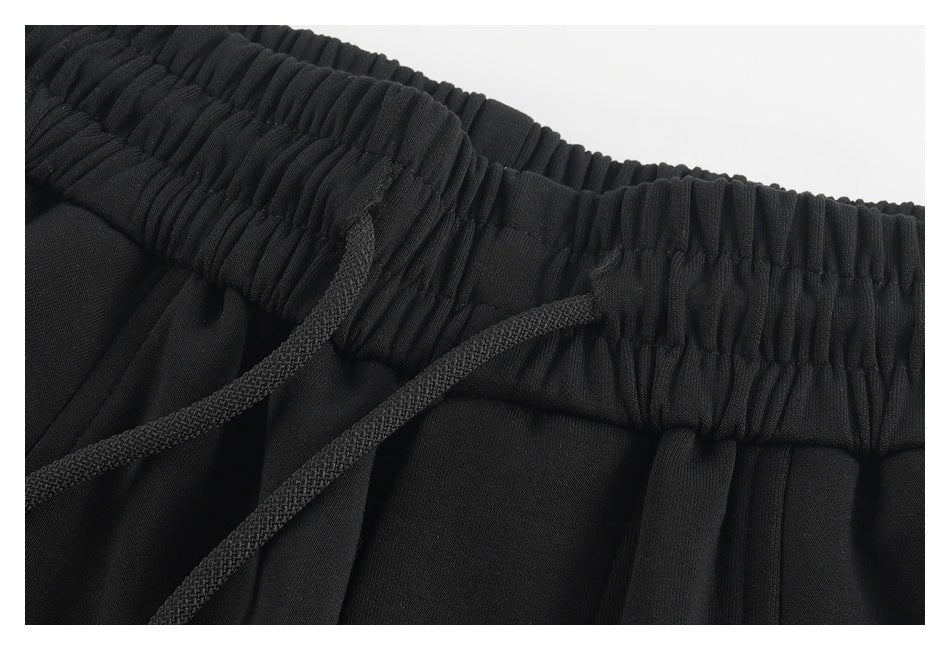 Close-up of black pants with a gathered elastic waistband and braided drawstring.