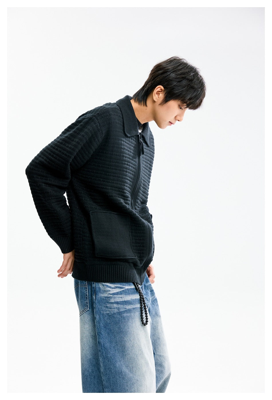 Side view of a model wearing a black textured zip cardigan with a wide collar and front pocket.