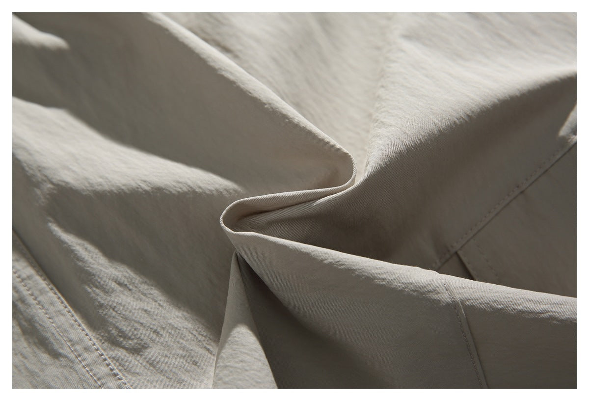 Close-up of light beige pants fabric gathered in folds, with visible stitching.