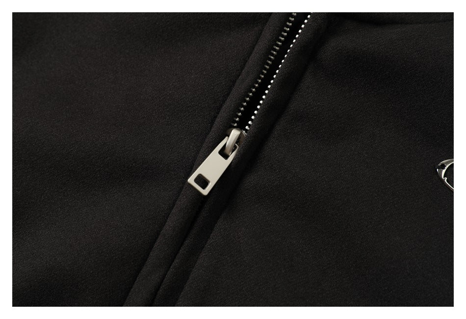 Close-up of a silver zipper and teeth on black jacket fabric, with part of an emblem at the edge.