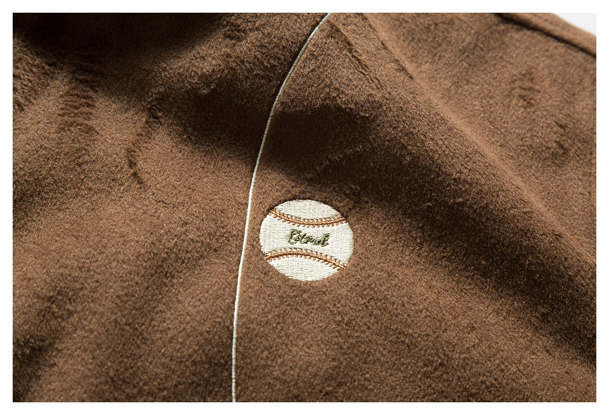 Close-up of a small embroidered cream badge on brown fuzzy jacket fabric beside light piping.