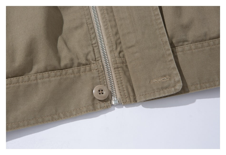 Close-up of a taupe jacket's lower front with a metal zipper, button, and stitched hem.