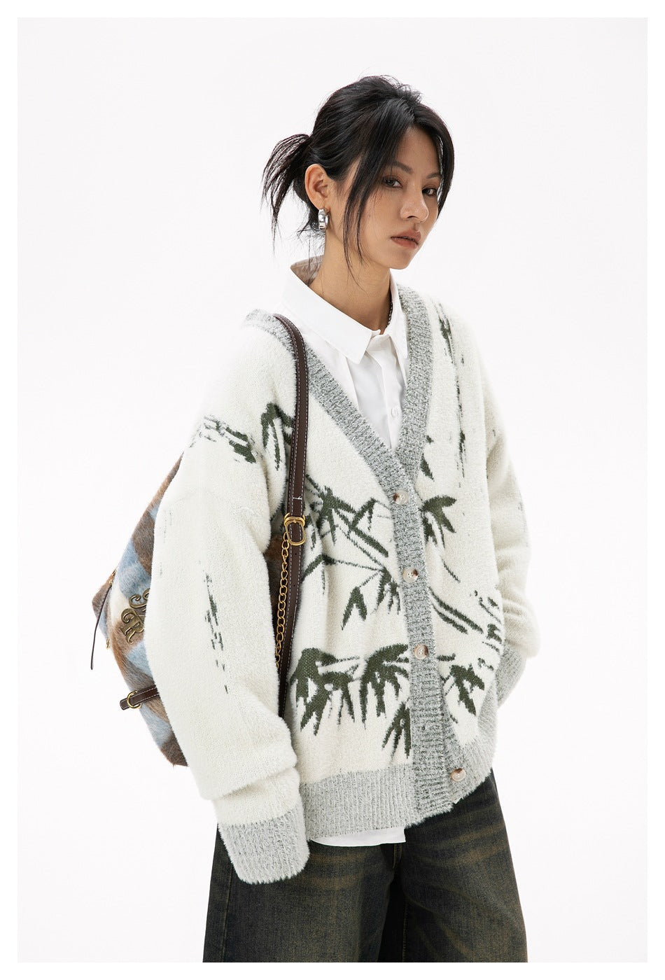 Three-quarter view of a model in an ivory cardigan with gray trim, buttons, and dark green abstract botanical motifs.