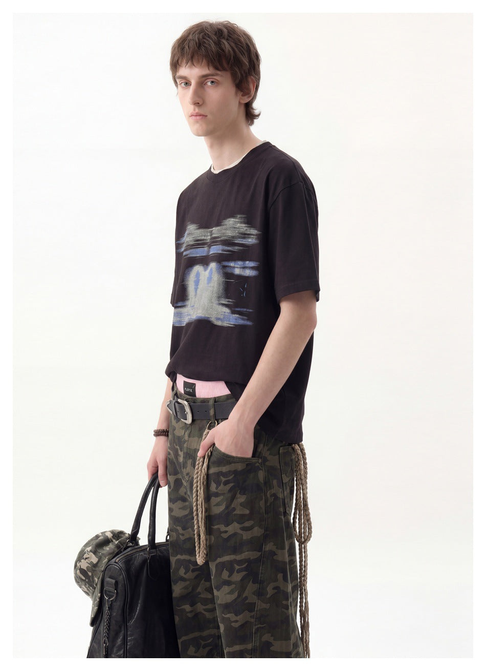 Close three-quarter view of a man in a black T-shirt with blurred blue and gray graphic and camouflage pants