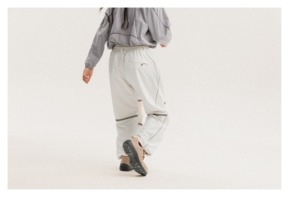 Rear view of a person wearing loose light-gray drawstring pants with dark reflective bands and a back pocket.