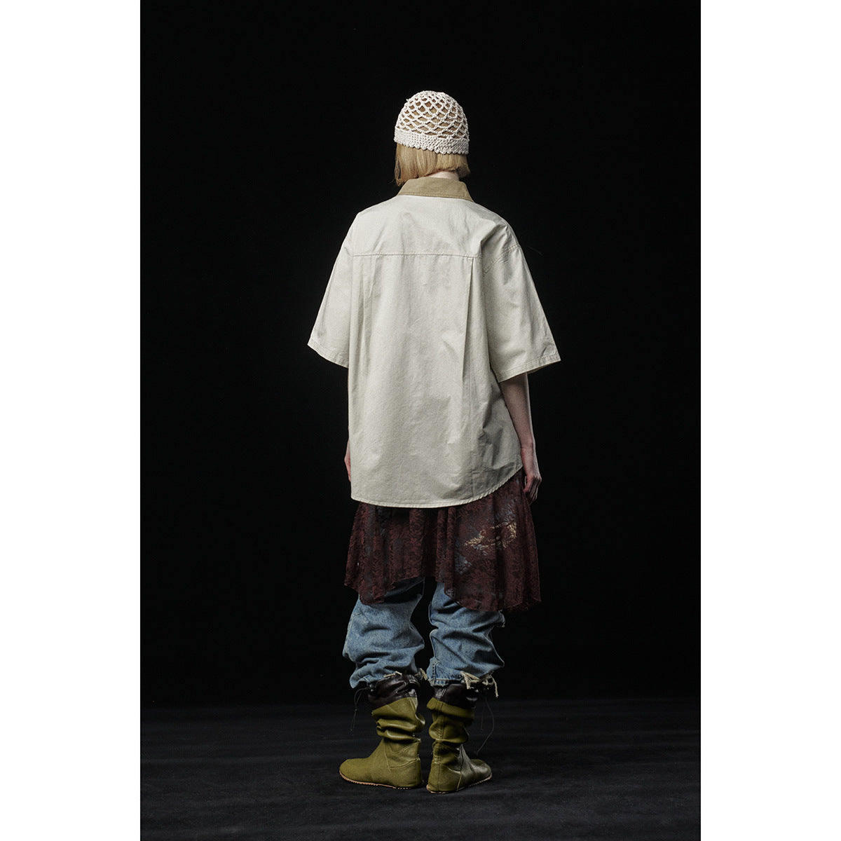 Back view of a model wearing the oversized cream short-sleeve shirt, patterned skirt, ripped jeans, and knit cap.