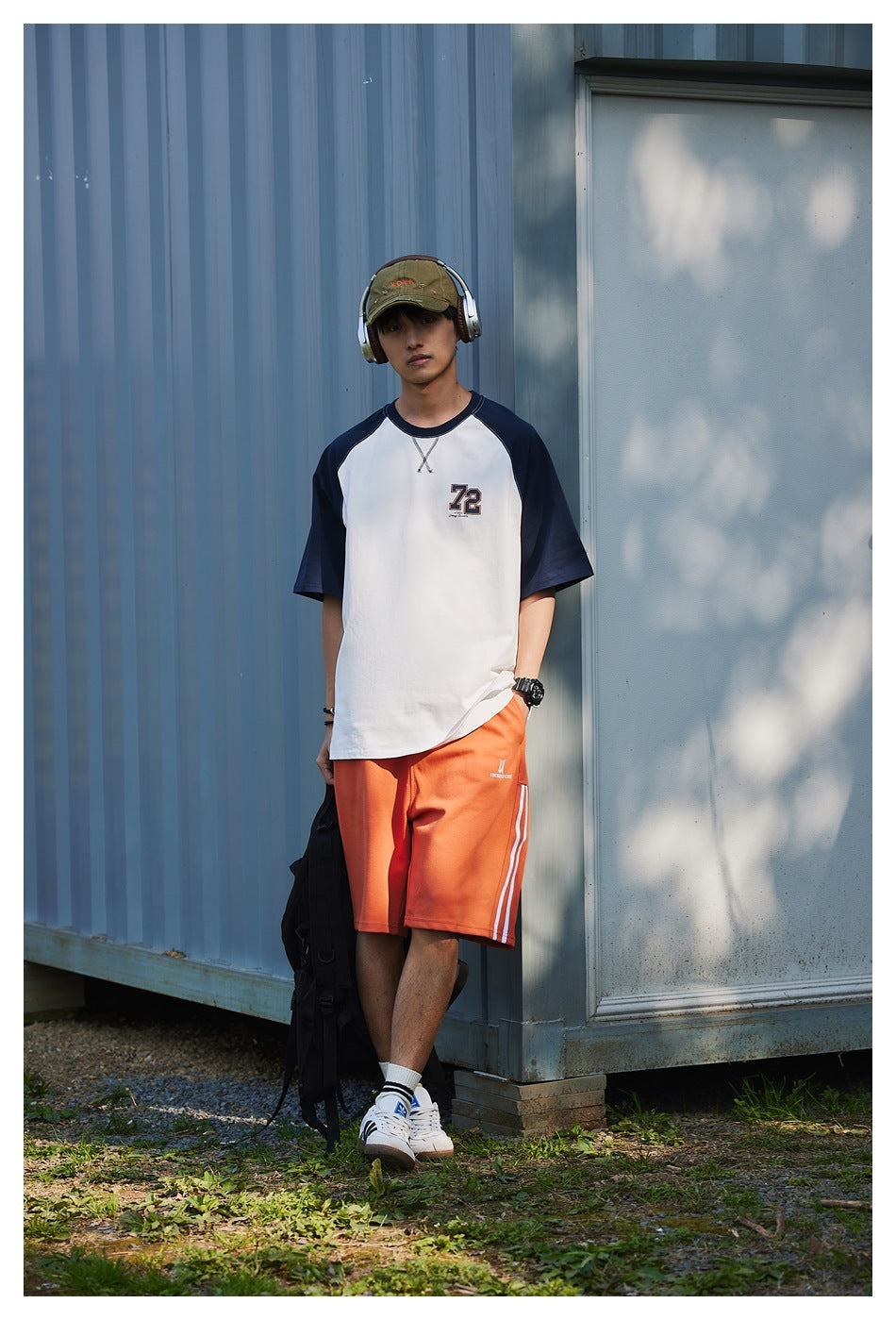 Model wearing a white raglan T-shirt with navy sleeves and a small 72 chest graphic, shown outdoors.