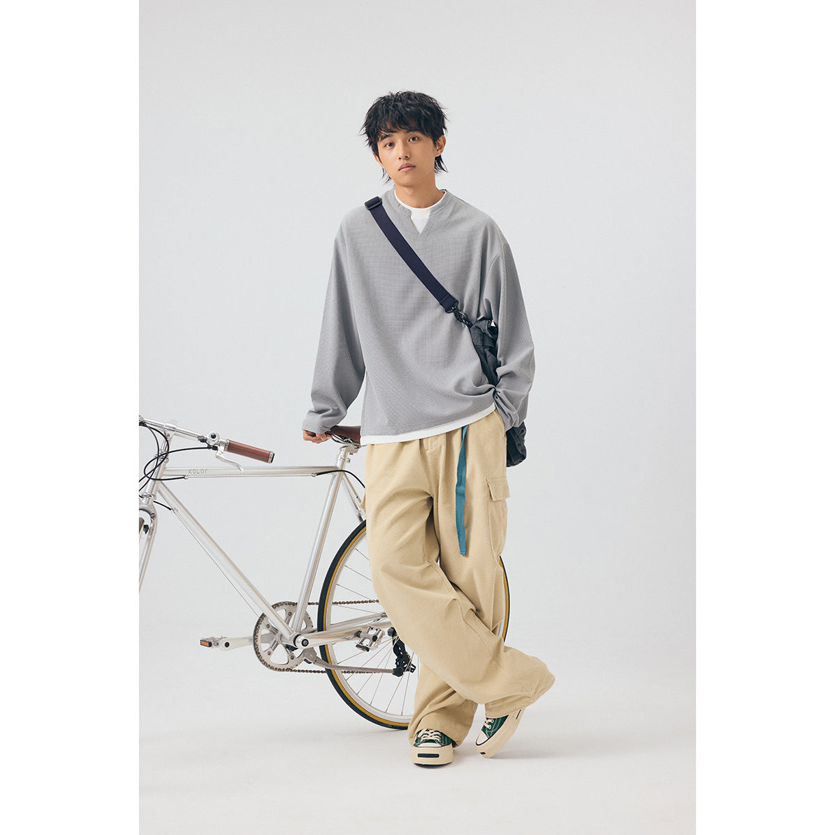 Model wearing a loose gray long-sleeve top and beige cargo pants beside a bicycle.