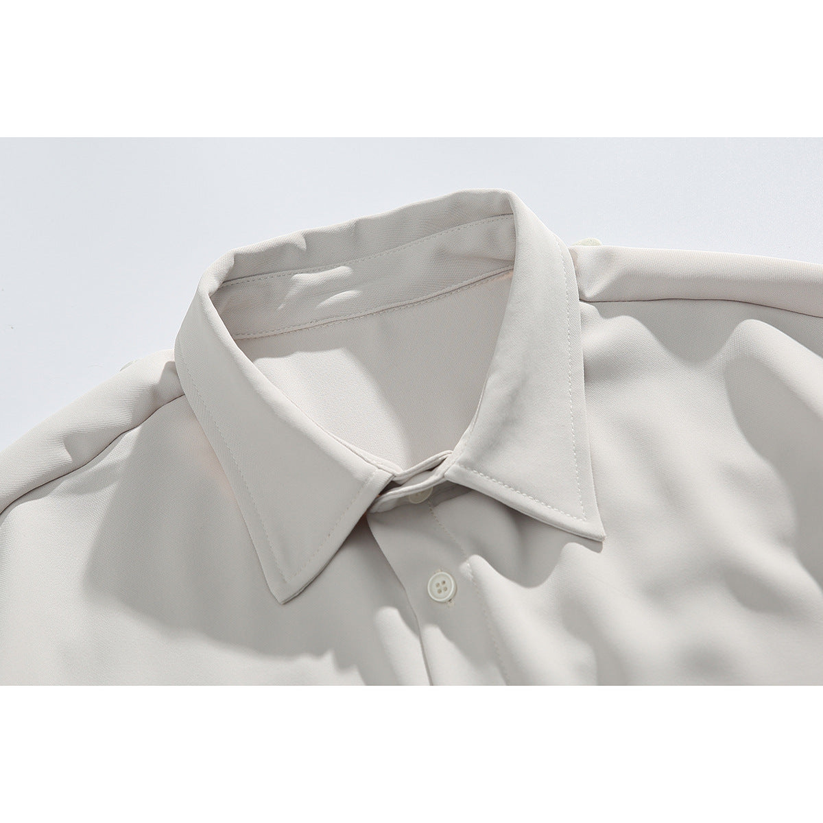 Close-up of an off-white button-up shirt collar, shoulder seams, and top button.
