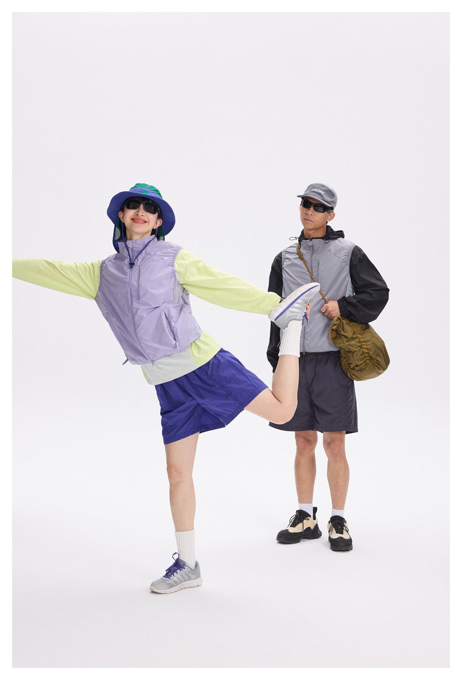 Two models pose in outdoor outfits: one wears a lavender vest and blue shorts, the other a gray vest and dark shorts.