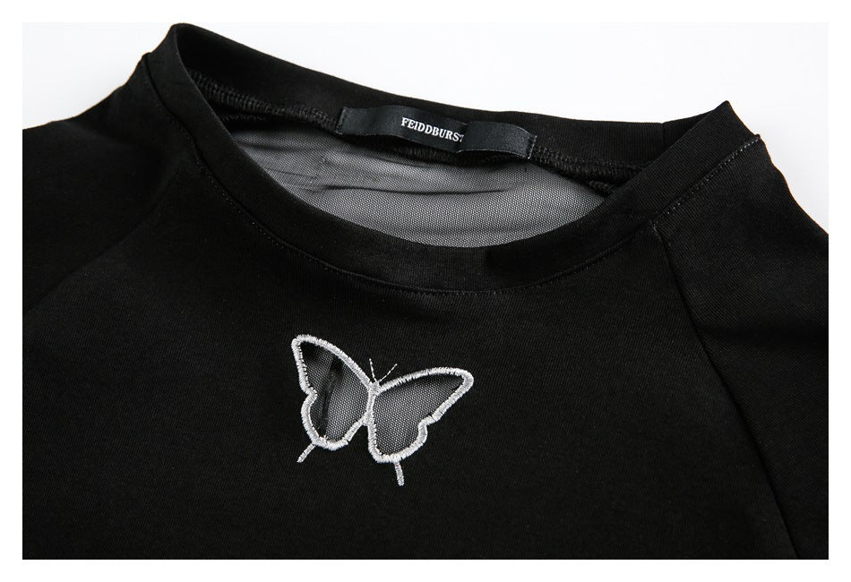 Close-up of the black top's neckline, sheer mesh panel, and small white embroidered butterfly.