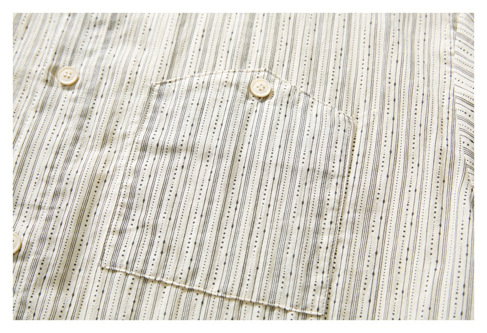 Close-up of the shirt’s chest pocket and buttons on ivory fabric with fine black dotted stripes.