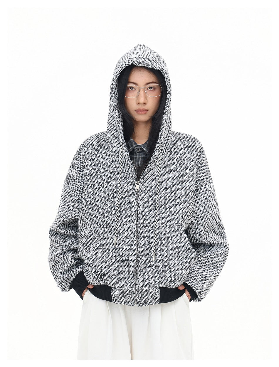 Front view of a model wearing a black-and-white patterned hooded zip-up jacket with black ribbed trim.