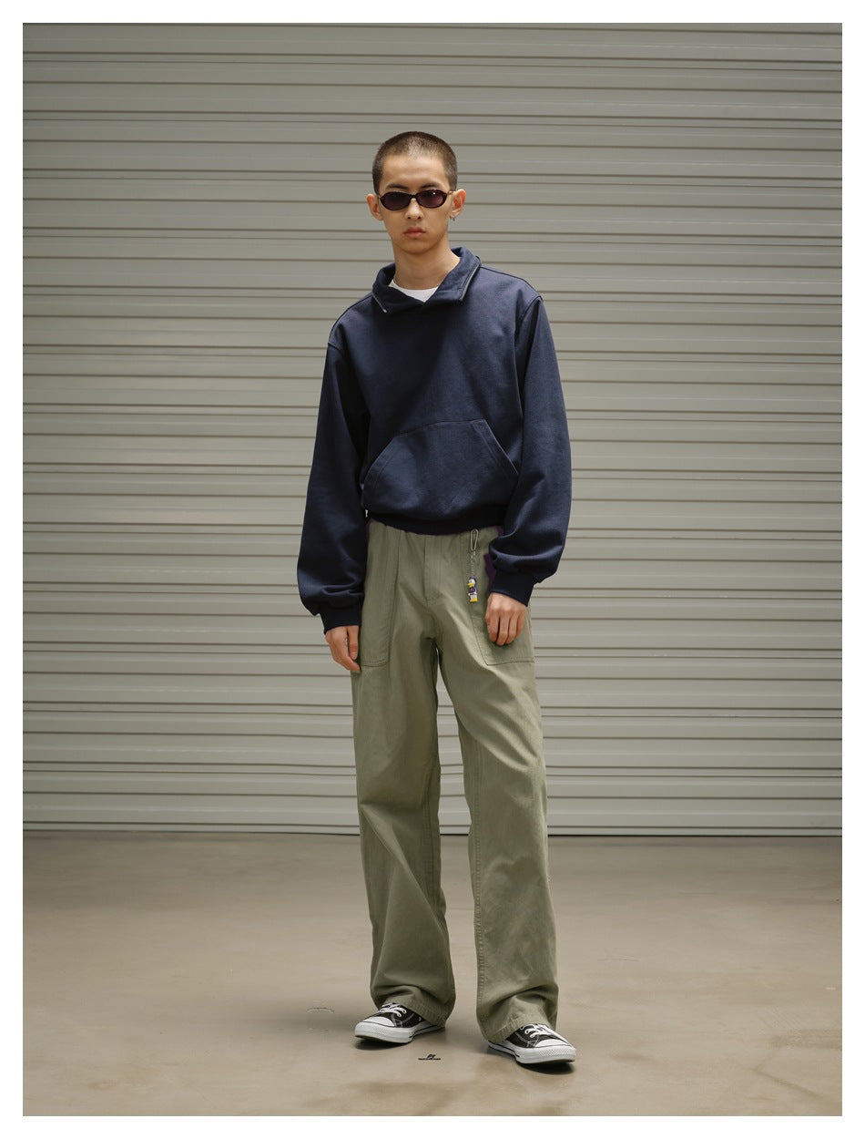 Model wearing olive green wide-leg utility pants with a navy pullover and black canvas sneakers, standing front view