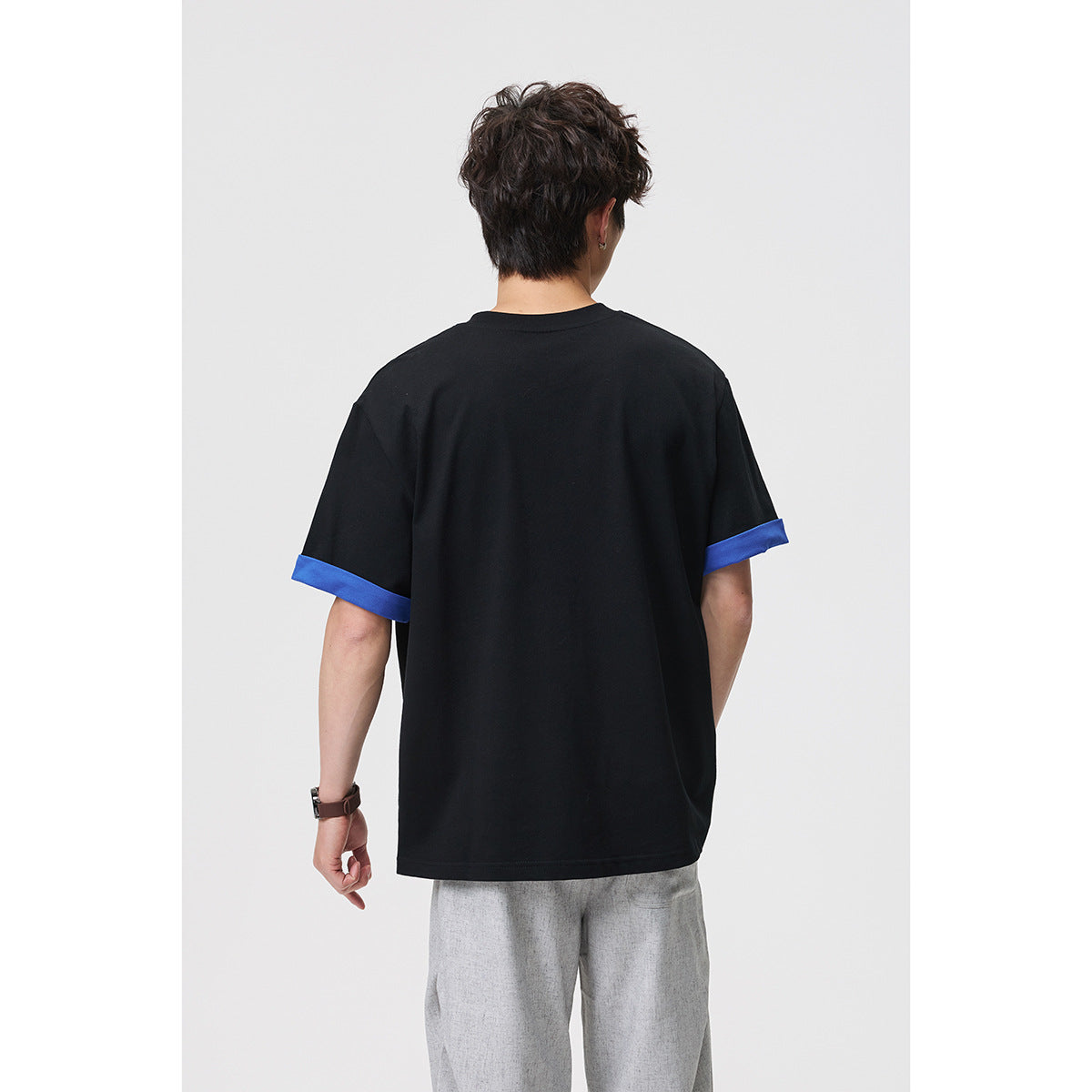 Back view of a model wearing a black shirt with bright blue rolled sleeve cuffs.