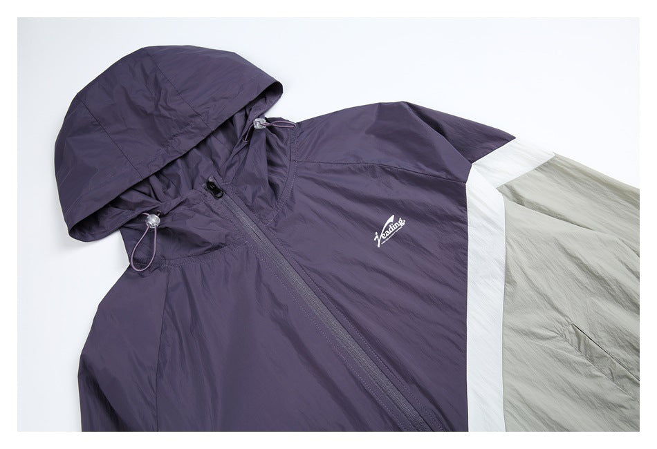 Angled close-up of the windbreaker’s purple hood, front zipper, chest logo, and white and pale gray color-block sleeve.