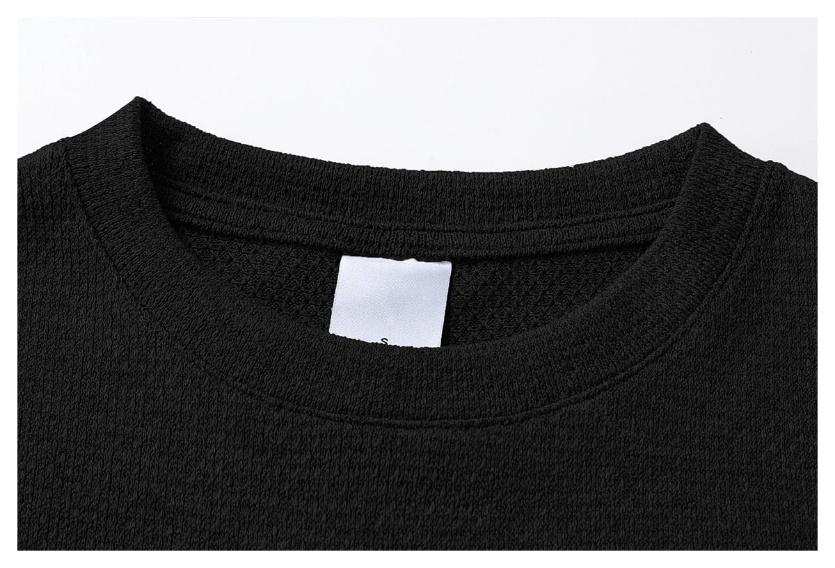 Close-up of a black shirt's crew neckline, textured fabric and a small white inner size label.