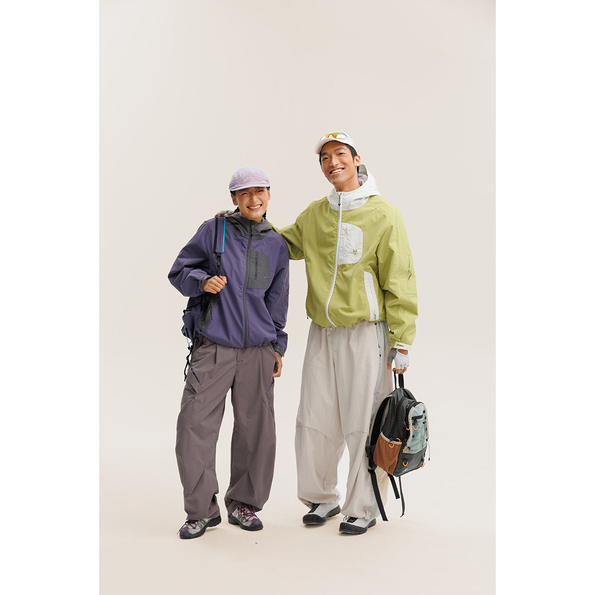 Two models wear color-block outdoor jackets and loose trousers; one jacket is purple and the other light green.