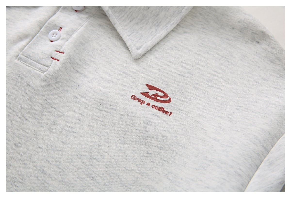 Close-up of a light gray heather polo shirt with a maroon chest graphic reading “Grab a coffee?”